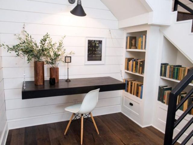 A small attic workspace with a dark stained floating desk and built in bookshelves