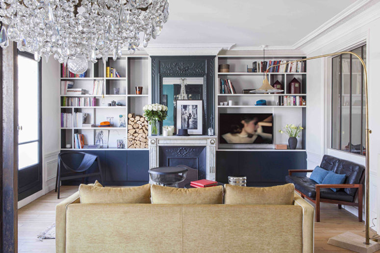 The living room is done with black ana navy touches, a faux fireplace, built-in storage shelves and eye-catchy furniture