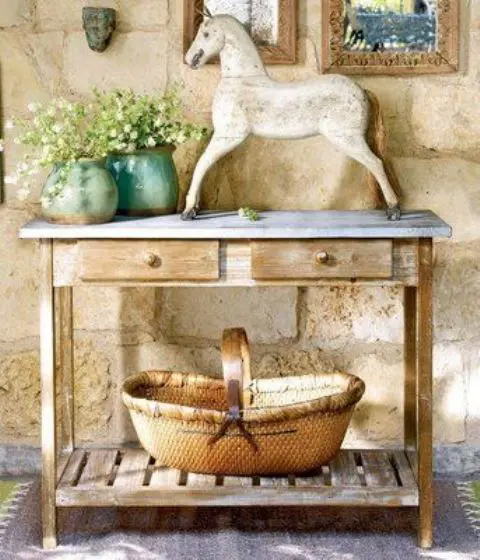 a rustic console table with a large basket, a statuette and some potted flowers