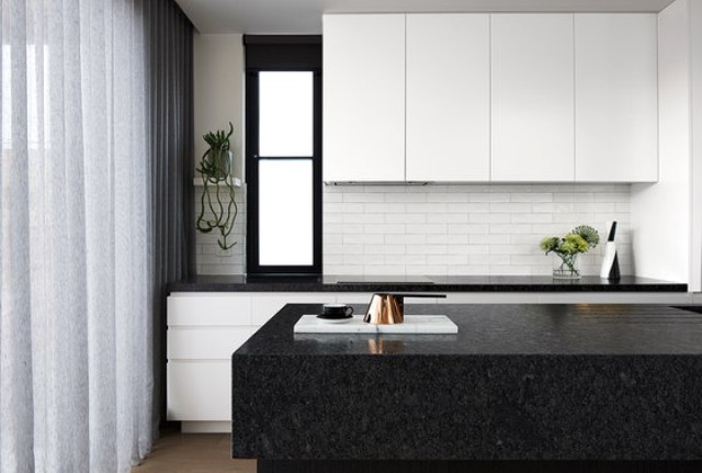 The kitchen is done with white cabinets and black stone countertops, the backsplash is of white brick