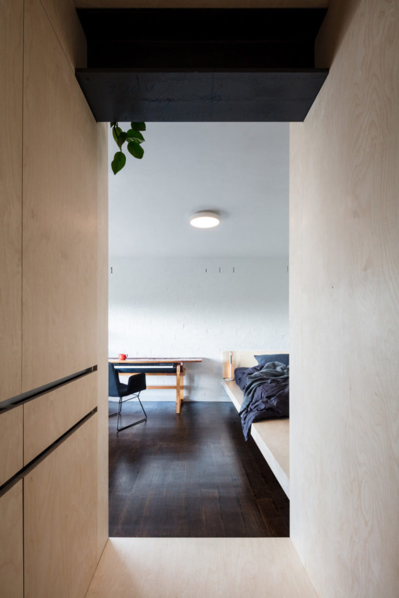 The interest is added to the space with a white brick wall, dark wooden floors that contrast the light-colored plywood