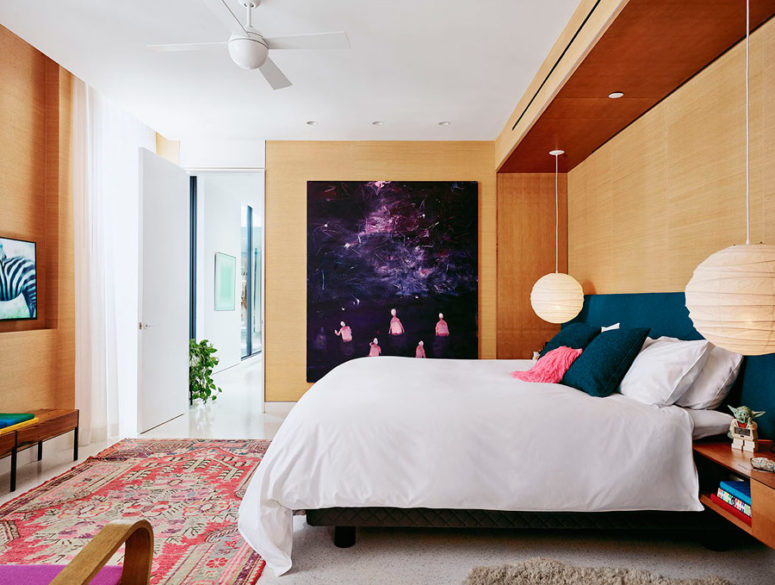 The master bedroom is done with light-colored wood, an upholstered wall and a very bold artwork that catches an eye