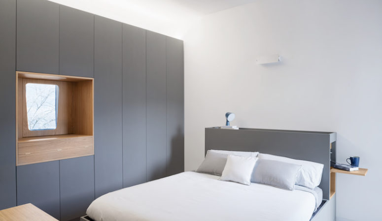 The master bedroom shows off a grey clad wall, a make up space, a grey bed with a storage headboard