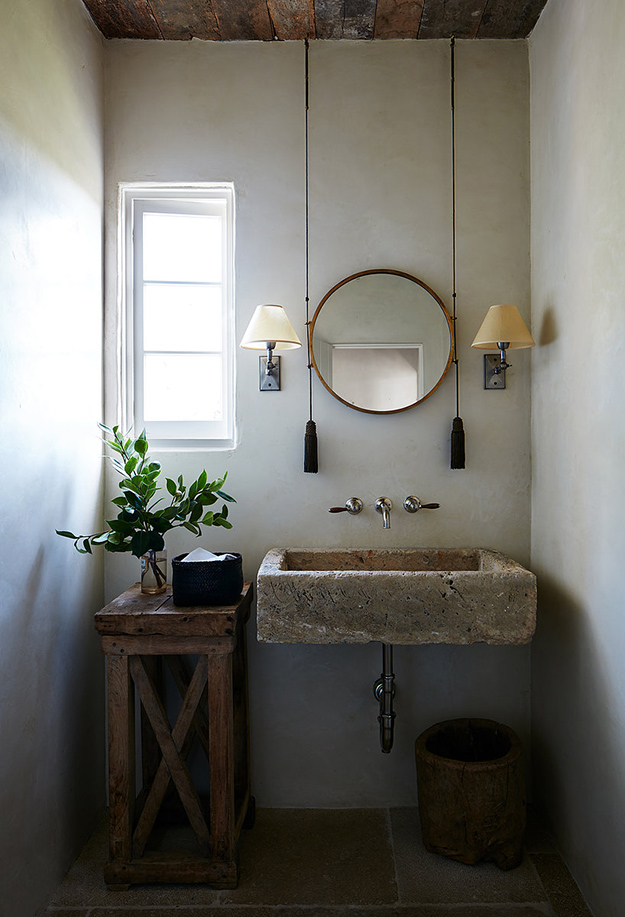 The bathroom is done with a stone sink, a wooden stand and bucket and some traditional sconces