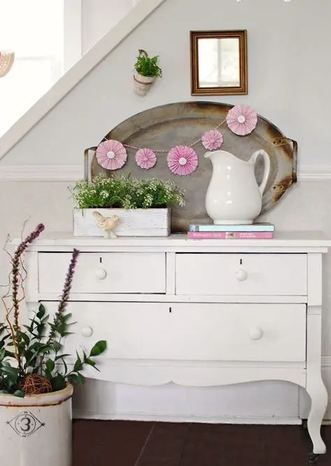 a vintage sideboard console, potted flowers and a cute pink paper fan garland