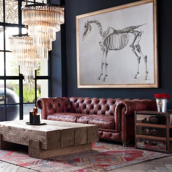 an eclectic space with a rough wooden beam table, glam crystal chandeliers and a brown leather Chesterfield sofa