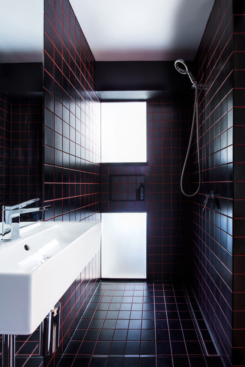 The bathroom is clad with black tiles and red grout for a stylish masculine inspired look