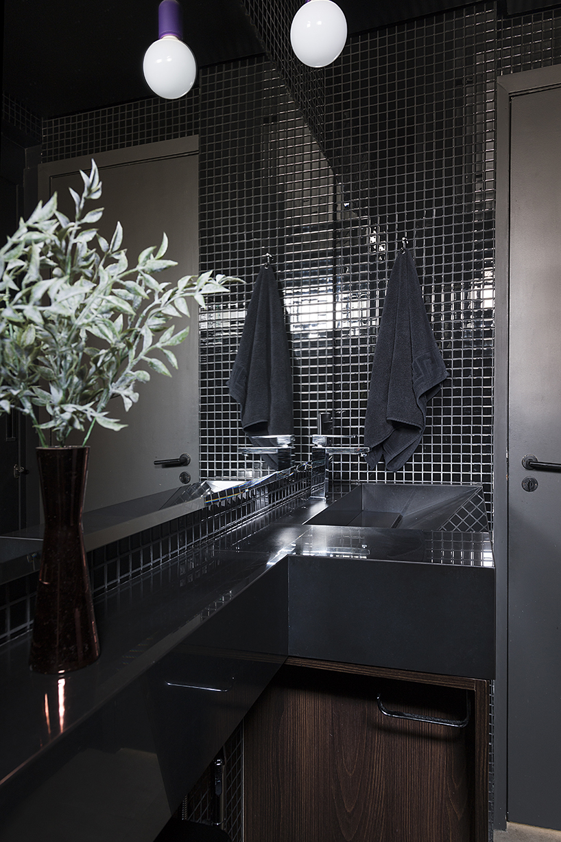The bathroom is clad with black tiles, white grout and there are black surfaces