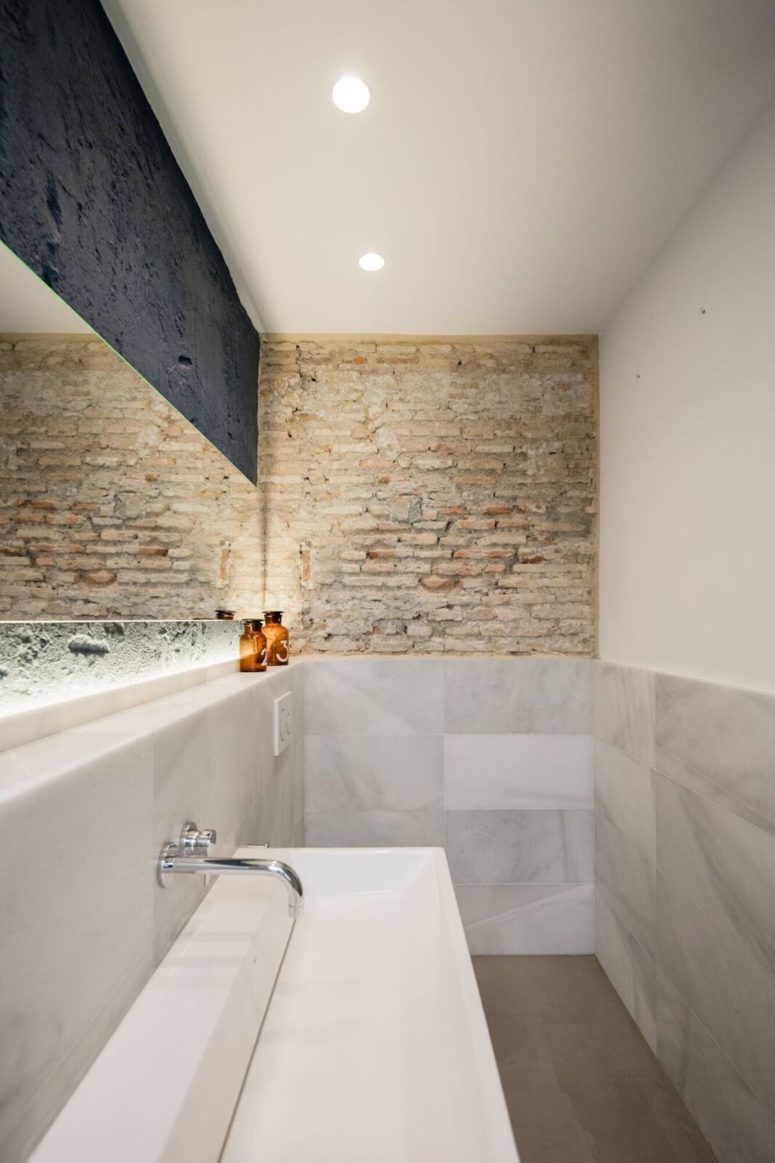 The bathroom also features exposed brick like everywhere else, built-in lights and marble
