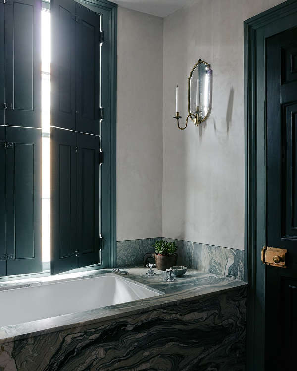 The bathroom features dark green shutters and a door and elegant marble surfaces