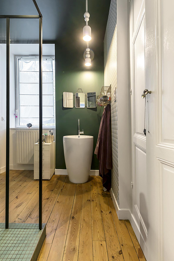 The bathroom is done with green and geometric wallpaper, wooden floors and a cool free standing sink