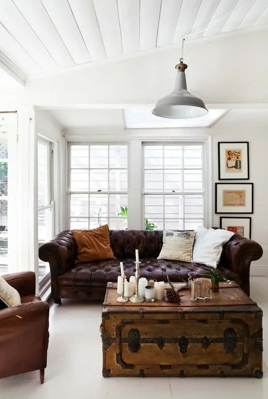 a creamy sunroom with dark leather furniture and a vintage chest for storage
