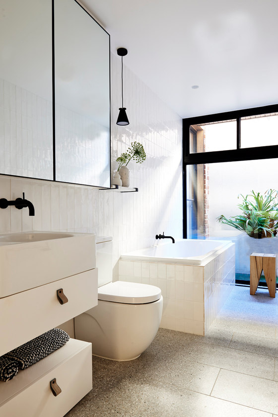 The bathroom is clad with creamy glossy tiles and accented with blacck details