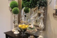 15 a console table with a boxwood wreath, moss balls on stands and lemons in a jar