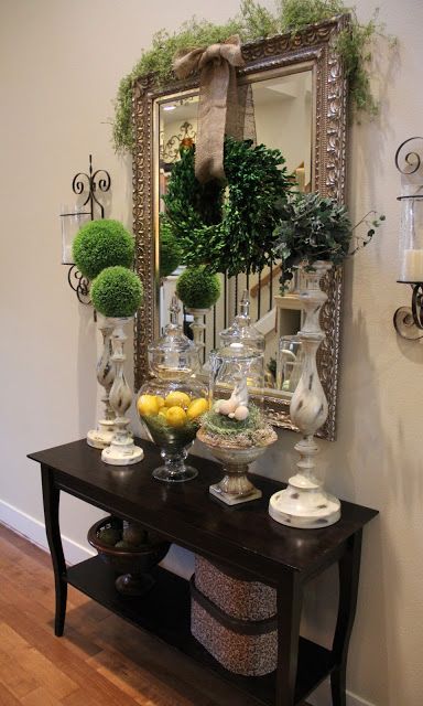 a console table with a boxwood wreath, moss balls on stands and lemons in a jar