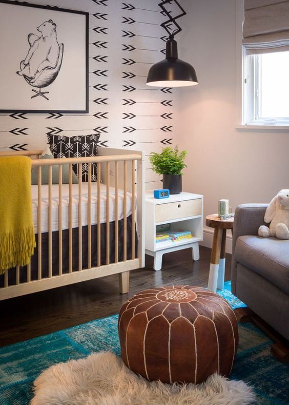 a boho nursery with a printed wall, a leather pouf and some rugs plus touches of color