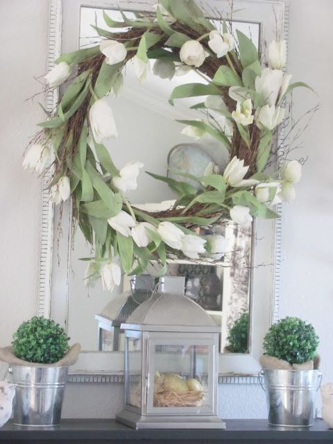 a wreath with white tulips, potted boxwood and a lantern with eggs in a nest