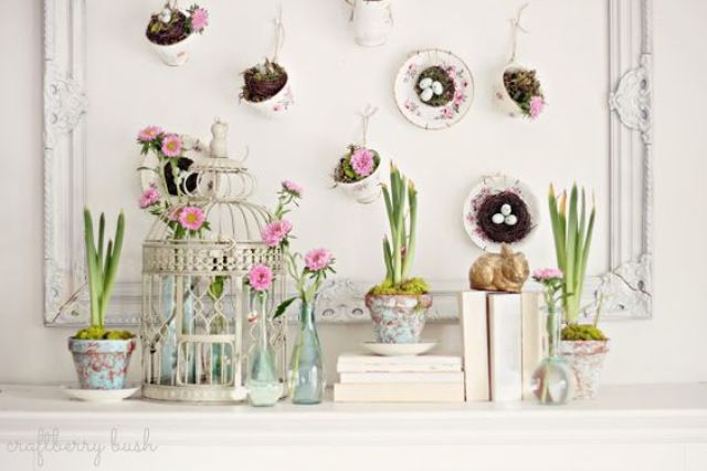 a bird cage with blooms, potted bulbs and an artwork with hanging cups with nests inside