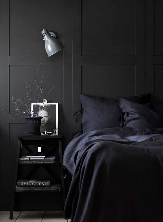 an all-black bedroom with a grey sconce as the only touch of a different color