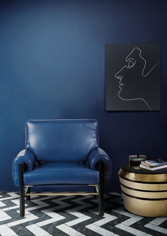 a navy wall and a matching leather chair plus a gold coffee table and an artwork create a very elegant look