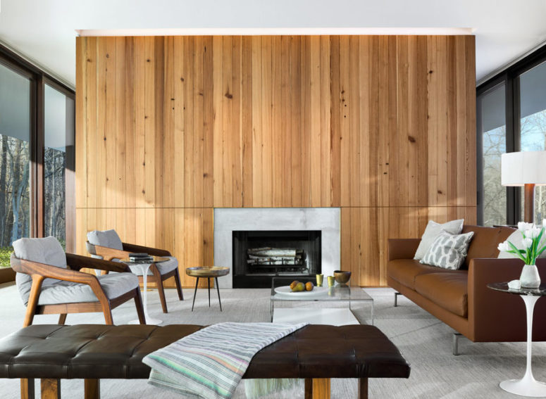 The living room of the house is done with a wood clad wall and a built in fireplace, there's chic mid century furniture and some contemporary touches, too