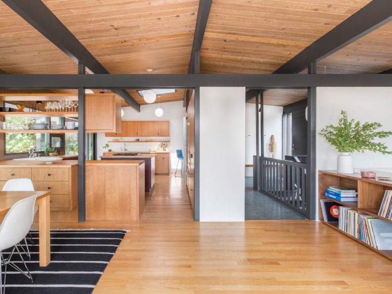 The main space is an open layout that comprises a kitchen, a dining room and a living space, it's clad with light-colored wood and there are dark exposed beams