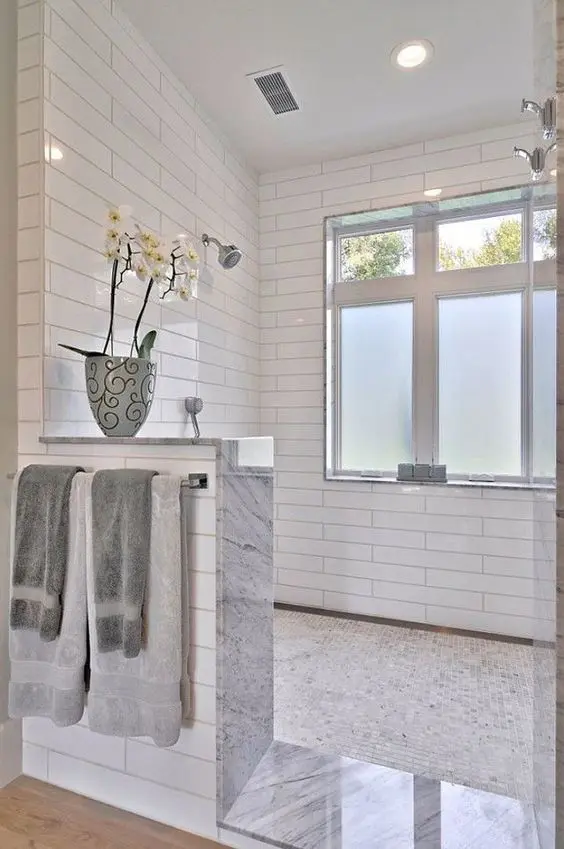 a large shower space is done with a pony wall and white orchids on them that add a luxurious feel