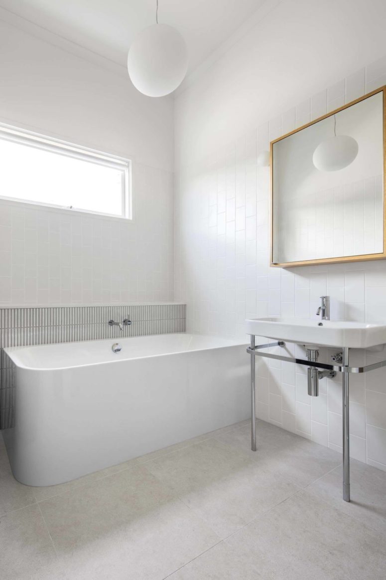The bathroom is white and sleek, there's a free-standing bathtub, white tiles and a modern mirror