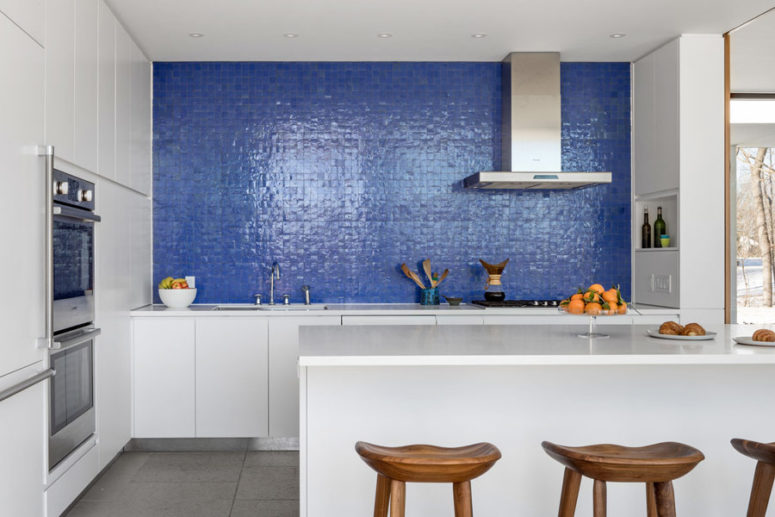 The kitchen is done with white cabinets and a kitchen island, and the backsplash wall is clad with purple tiles