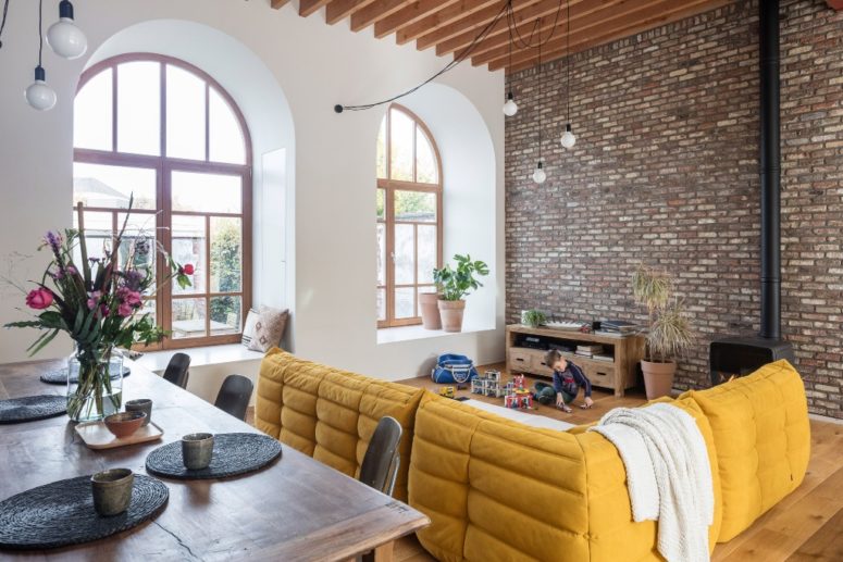 The dining space is created with an industrial dining set, metal chairs and a wooden table, the living room is defined with a bold yellow L-shaped sofa