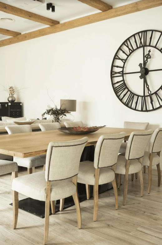 The dining space is done with a wooden dining table, comfy upholstered chairs and a large vintage clock
