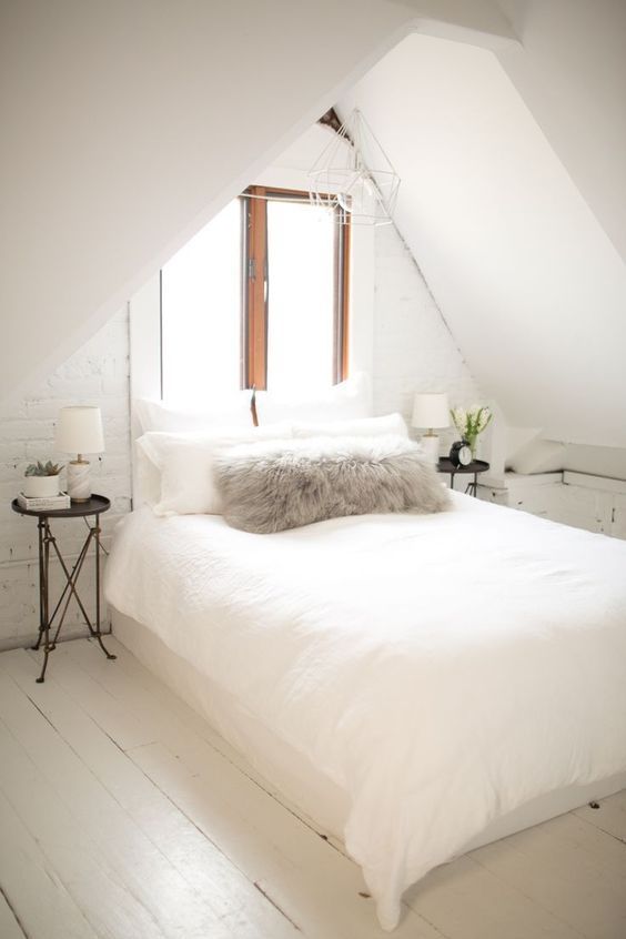 a neutral attic space with a bed in the center and little nightstands on both sides