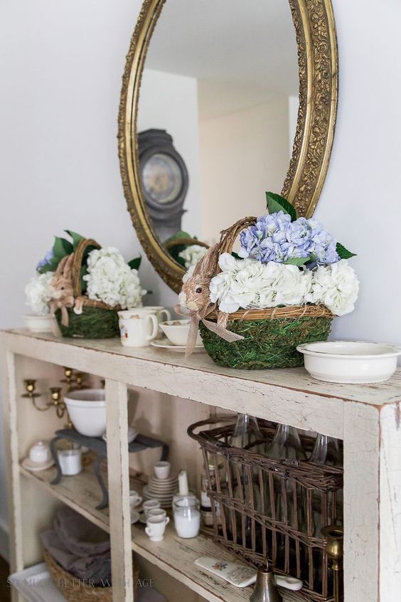 a shabby chic console with moss baskets with bunny faces and hydrangeas