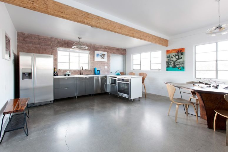The kitchen and dining space comprise one space with wooden beams, an exposed brick wall and metal cabinets