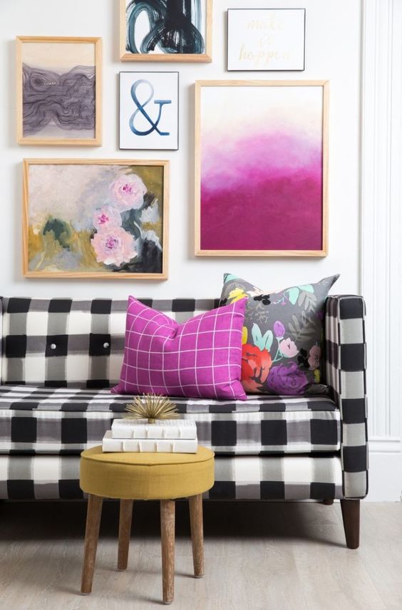 a black and white buffalo check sofa is brightened up with a lot of colorful artworks over it