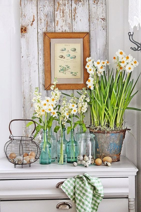 a console styled with fresh blooms in clear vases and a bucket, a nest with real eggs