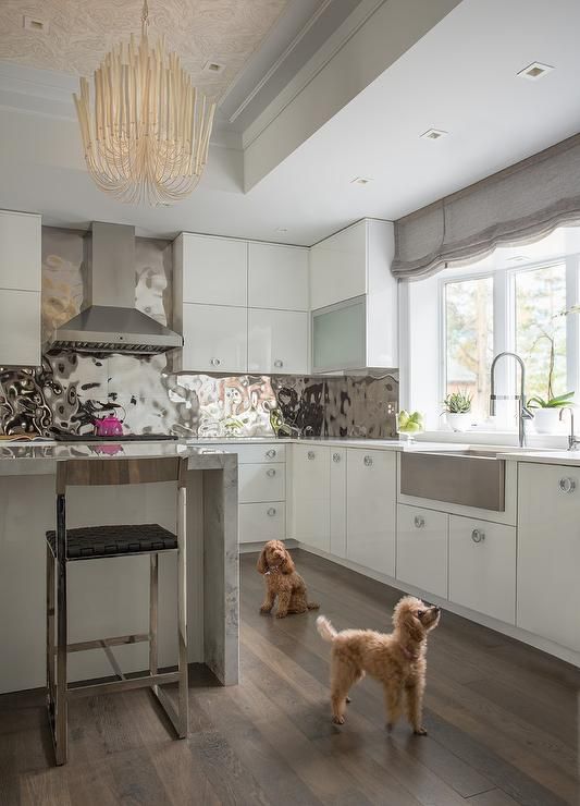 a polished hammered metal backsplash adds a glam feel to the white and grey kitchen