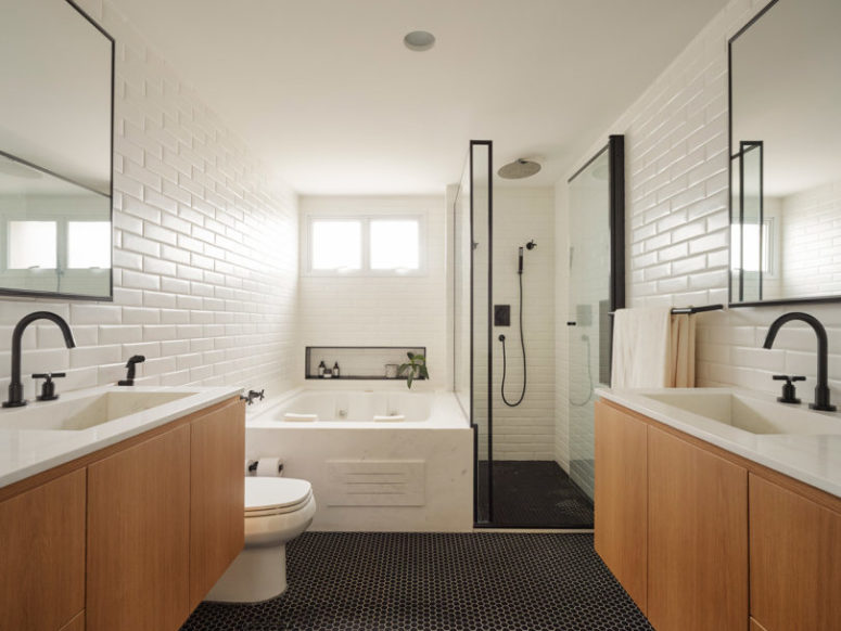 The master bathroom is done with white tiles, black penny ones on the floor and light-colored wood