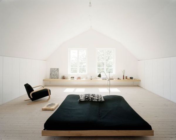 an airy minimalist attic bedroom with a bed in the center, a windowsill shelf and a chair