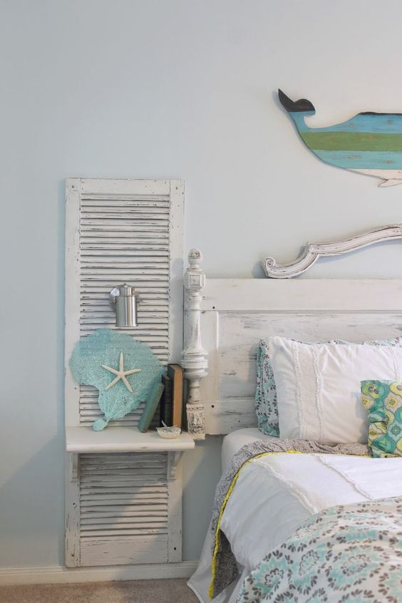 A wall mounted nightstand for a shabby chic beach bedroom is made of an old shutter and a piece of wood