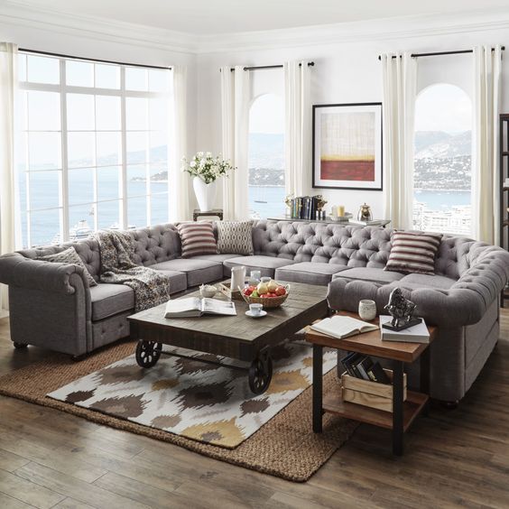 A modern farmhouse living room with a grey U shaped tufted sofa and some rustic tables