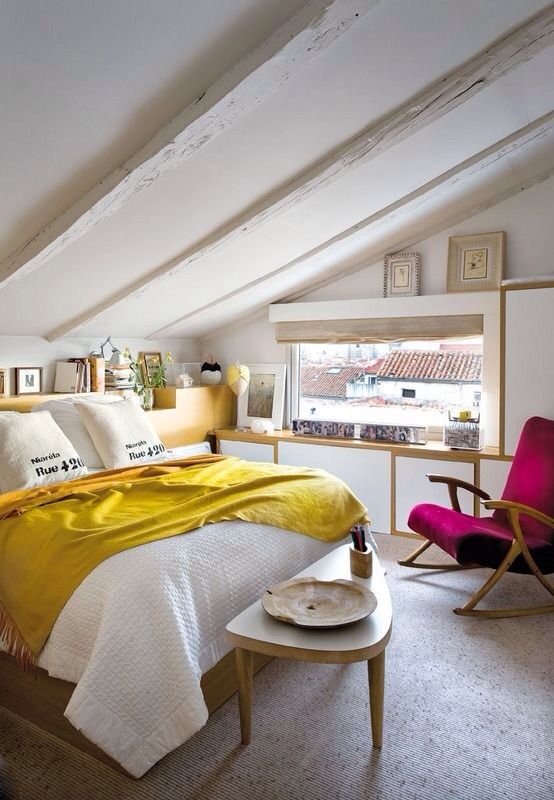 a small and colorful attic bedroom with a bed in the center and an armchair in the corner
