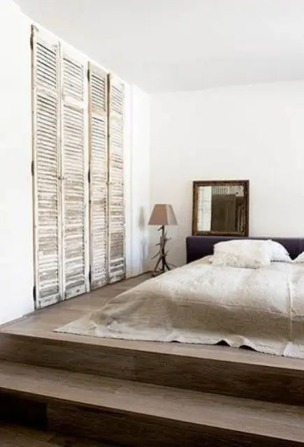 a minimalist sleeping space with old shutters as wardrobe doors that add texture and interesting to the space