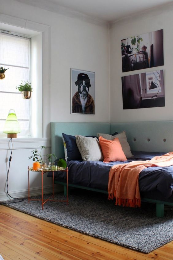 a small and colorful bedroom with a mint bed with a corner headboard and bold touches