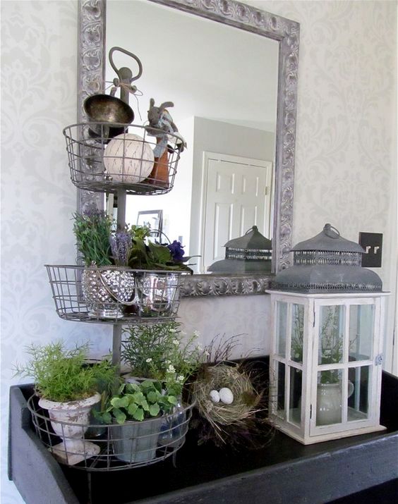 a console with a faux nest with eggs, a lantern and a stand with potted greenery and flowers