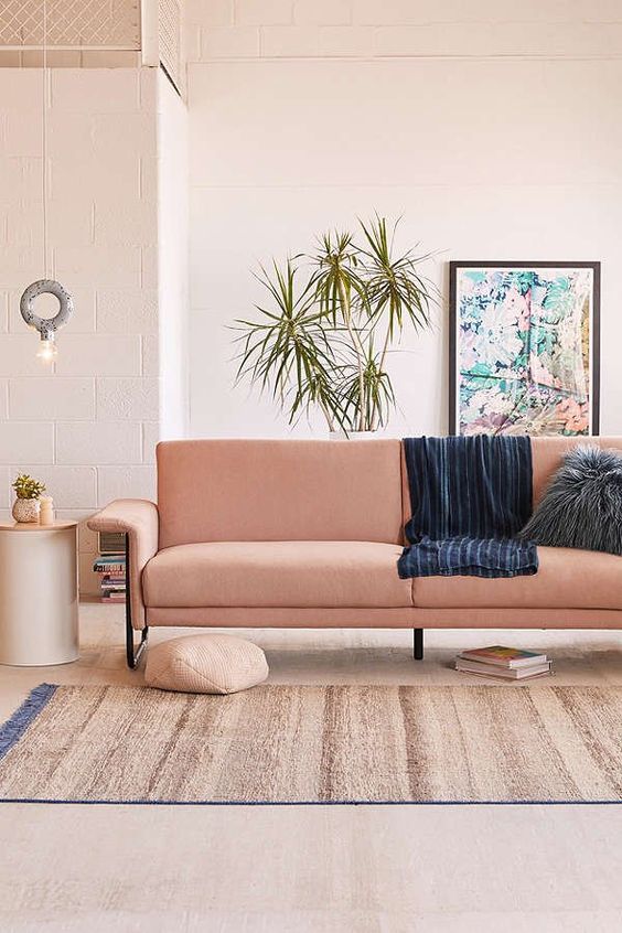 A cozy warm colored living room with a salmon colored sofa and potted greenery feels like summer