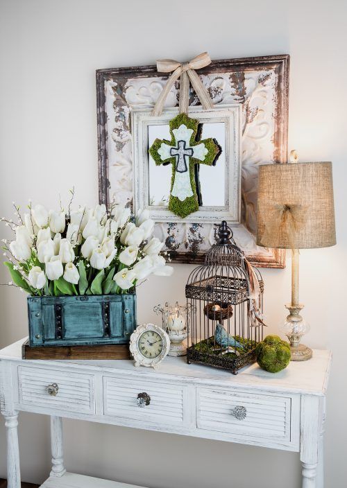 a shabby chic white console with white tulips and willow pussy in the box, a birdcage with a faux nest and bird and a moss cross