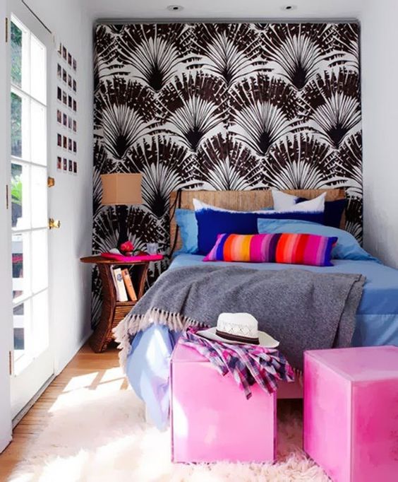 a tiny yet colorful bedroom with a printed wall, colorful cube ottomans and bold bedding