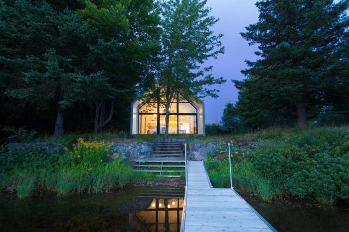 The cottage is built of wood with a single gable roof and a fully glazed wall that faces the lake