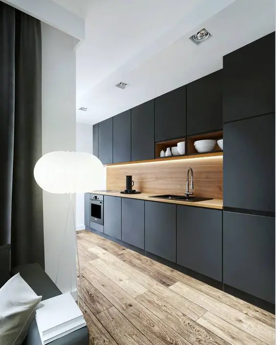 a black kitchen is made more interesting with a light-colored wood backsplash and an aged wood floor